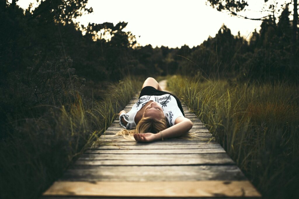 A serene scene of a woman relaxing on a wooden pathway amidst lush greenery, conveying tranquility.